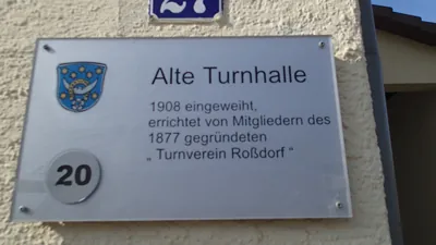 Schild an der Alten Turnhalle: „1908 eingeweiht, errichtet von Mitgliedern des 1877 gegründeten Turnverein Roßdorf“