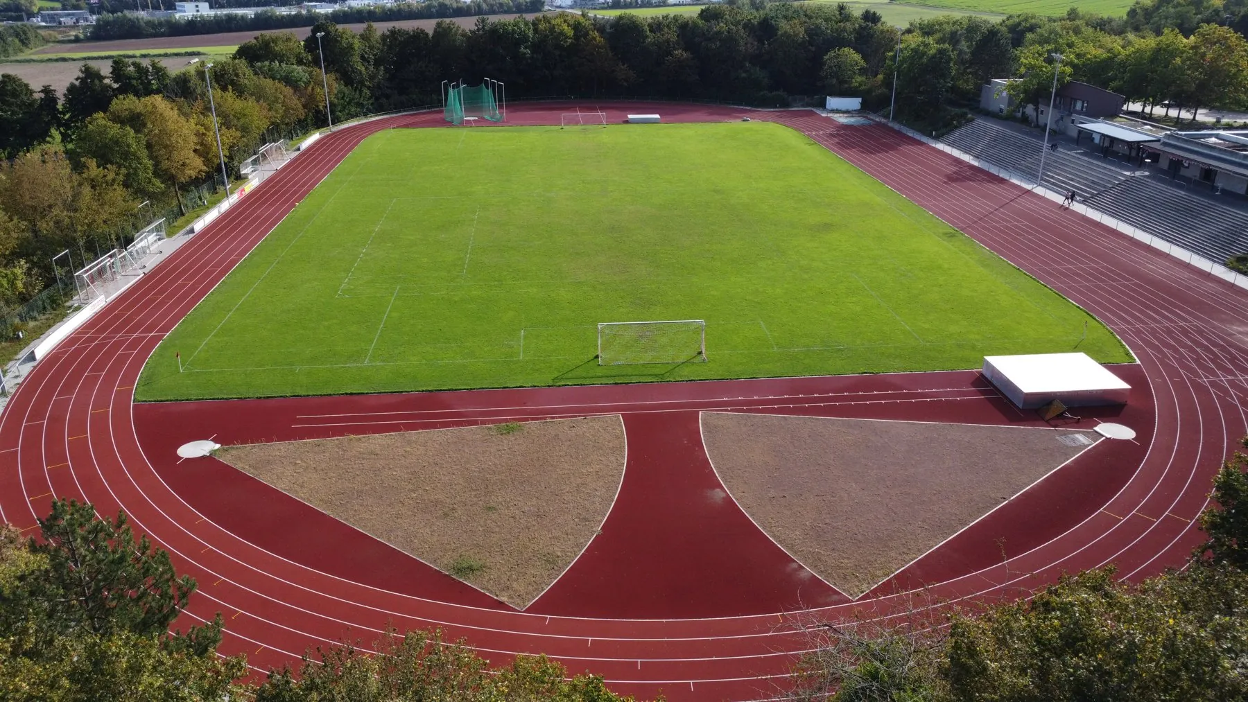 Luftbild des Stadions im Sportzentrum am Zahlwald: Rasenplatz, rote Rundbahn, Tribüne und Wald